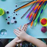 playdough, googly eye and pipe cleaners on table with kids hands